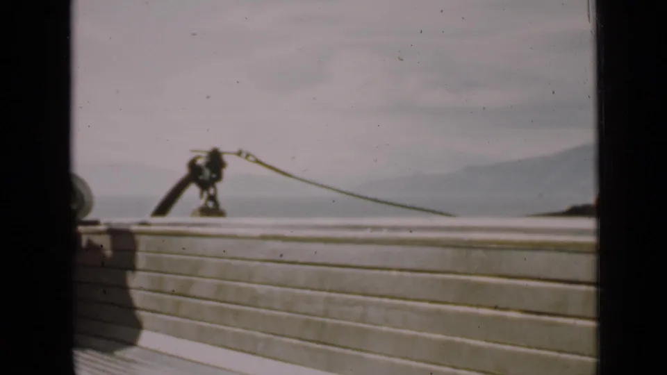 Vintage 8mm boat-deck view in San Francisco, with railing, rope hardware, calm water, and hazy hills.