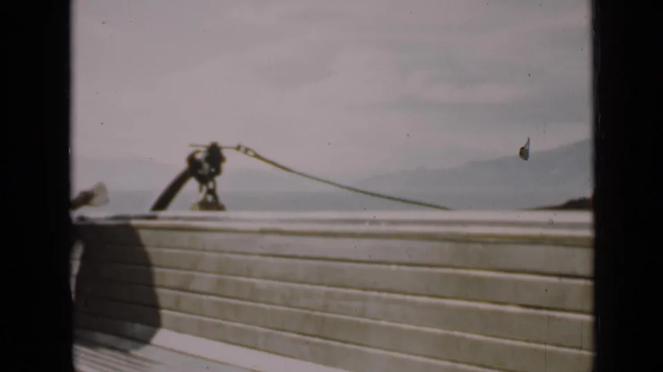 1939 San Francisco boat-deck frame showing railing, rope hardware, bay water, hazy hills, and cloudy sky.