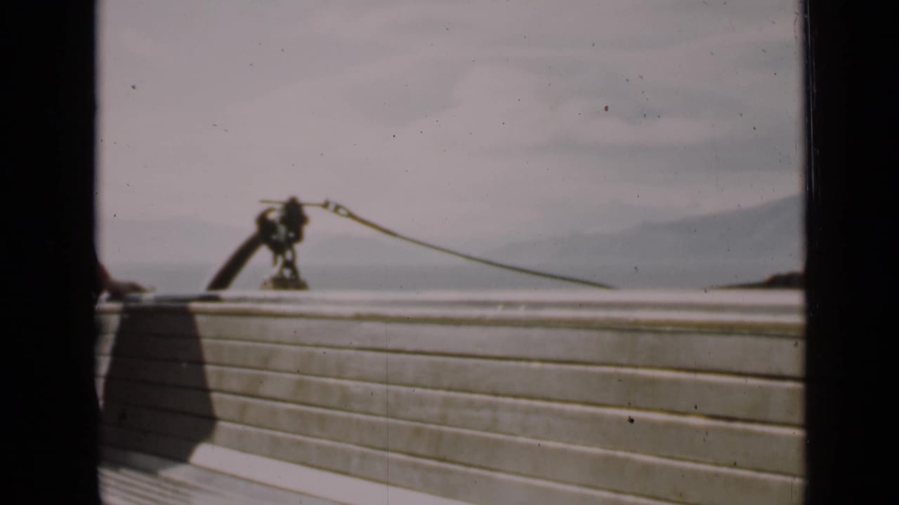 Wooden deck rail with rope hardware, water, and distant hills seen through dark film-frame edges.