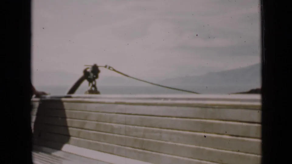 1939 San Francisco harbor view from a vessel, showing deck rail, rope hardware, water, and distant shoreline through dark frame edges.