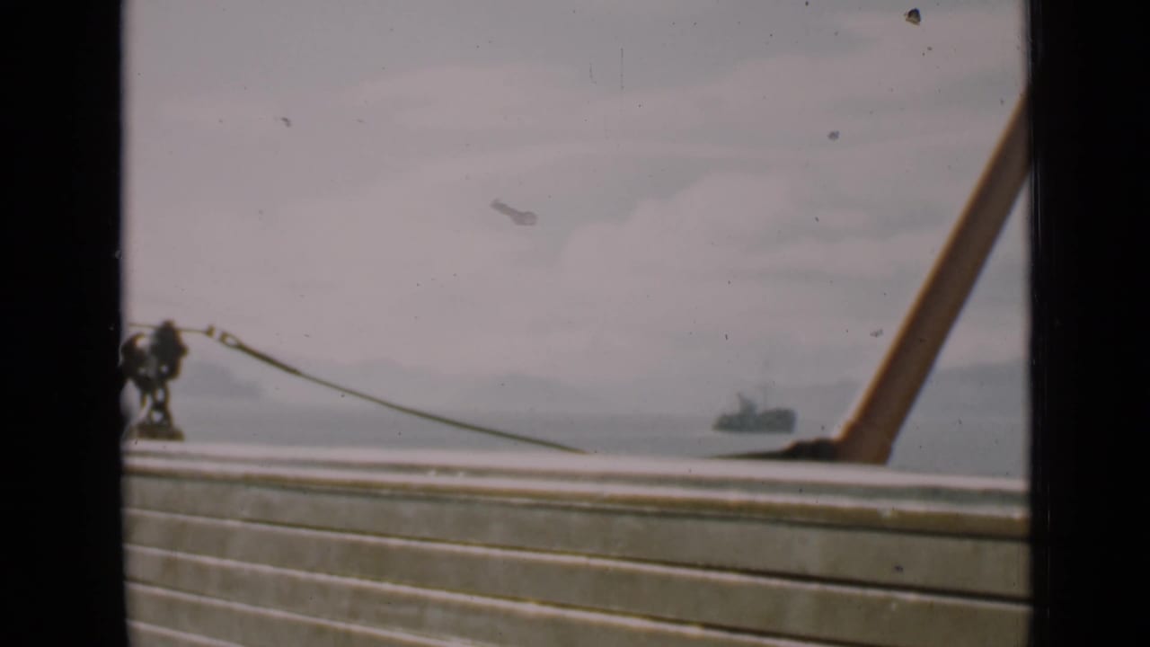 Boat railing and mooring hardware with bay water and a distant tugboat beyond.