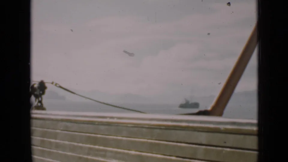 1939 San Francisco home-movie frame looking past a boat railing and mooring hardware toward bay water and a distant tugboat.