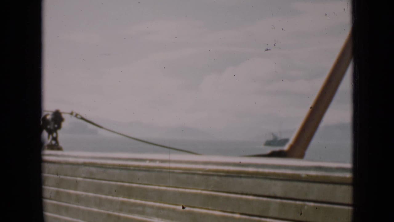 1939 San Francisco frame showing a boat deck rail in the foreground, bay water, hazy shoreline, and a distant vessel.
