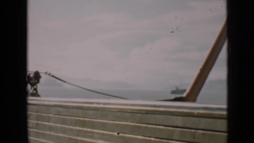 1939 San Francisco frame showing a boat deck rail in the foreground, bay water, hazy shoreline, and a distant vessel.