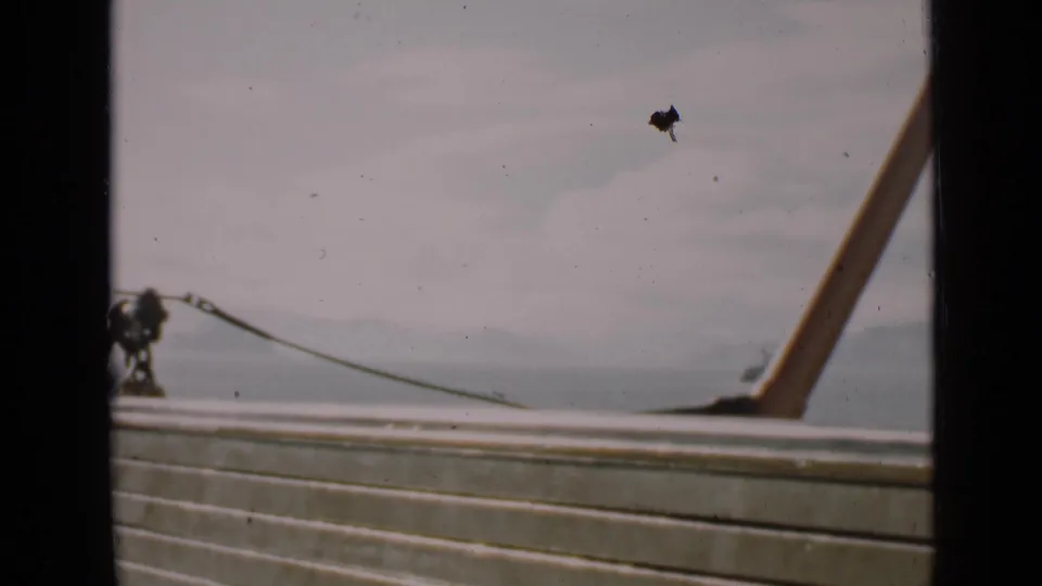 1939 San Francisco home-movie frame with a boat railing, slanted deck support, pale bay water, and hazy shoreline.