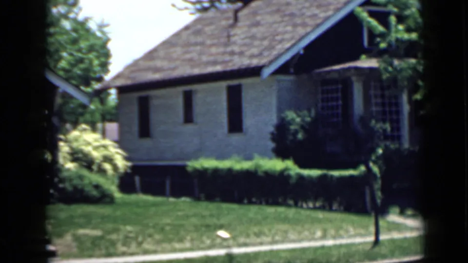 1939 San Francisco home-movie frame showing a brick house exterior with lawn, shrubs, walkway, and surrounding trees.