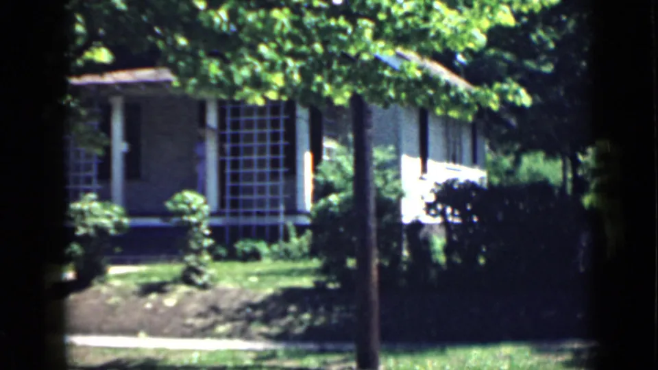 1939 San Francisco home-movie view of a house and garden, with gridded window, hedges, lawn, walkway edge, and tree shade.