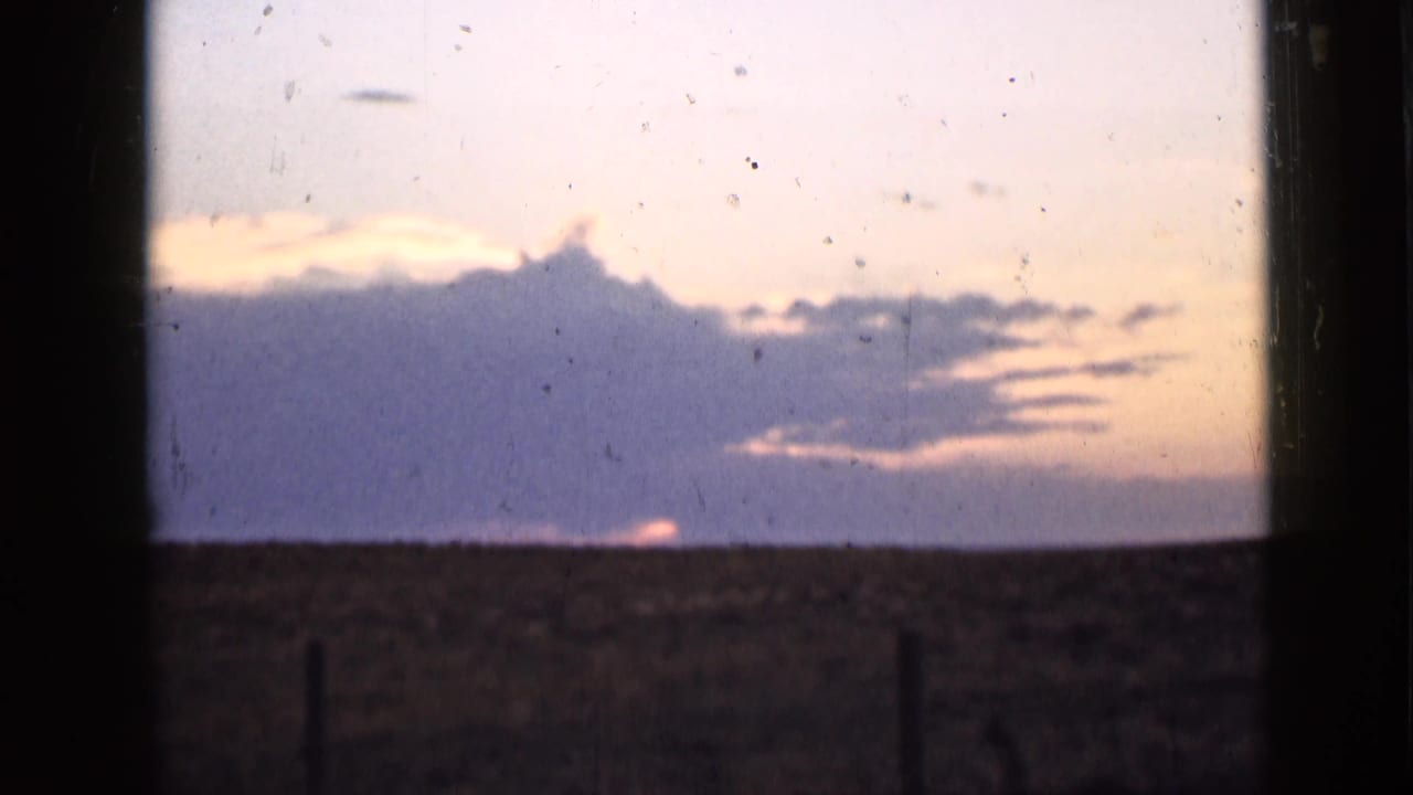 Large cloud bank over a dark open landscape with sunset color near the horizon.