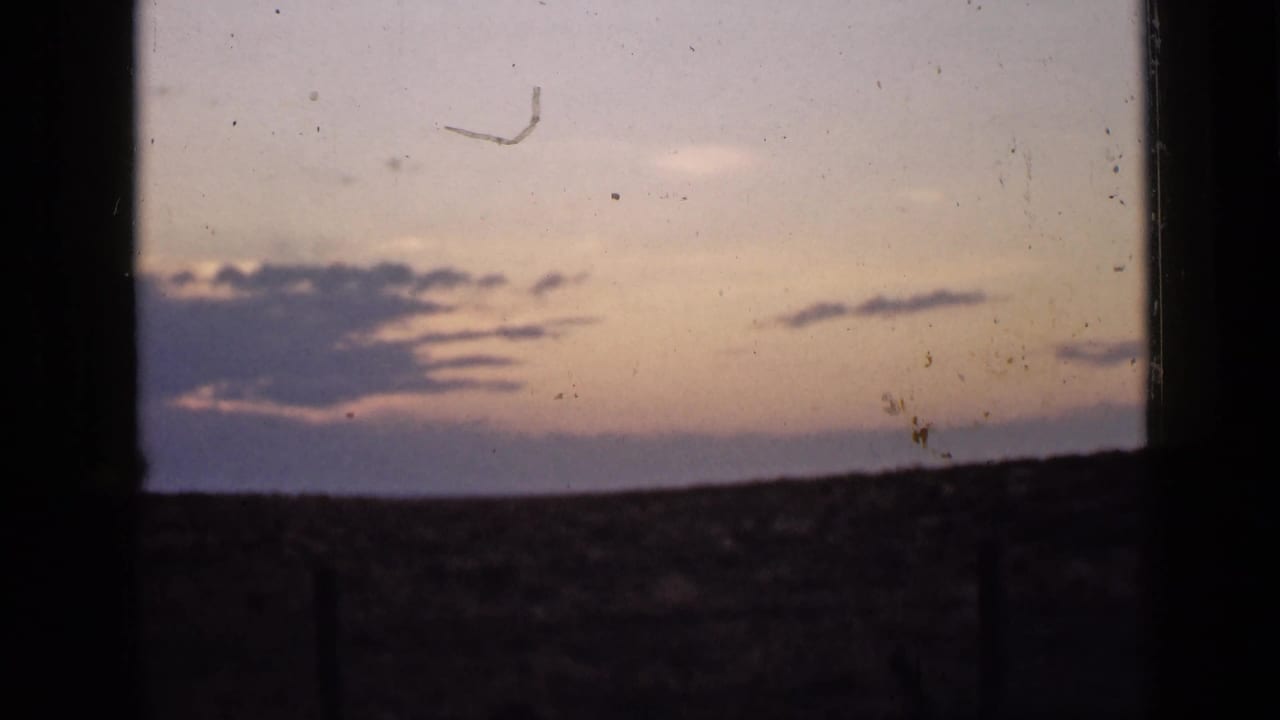 Dusk horizon seen through dark vertical framing, with pink sky above a shadowed rural plain.