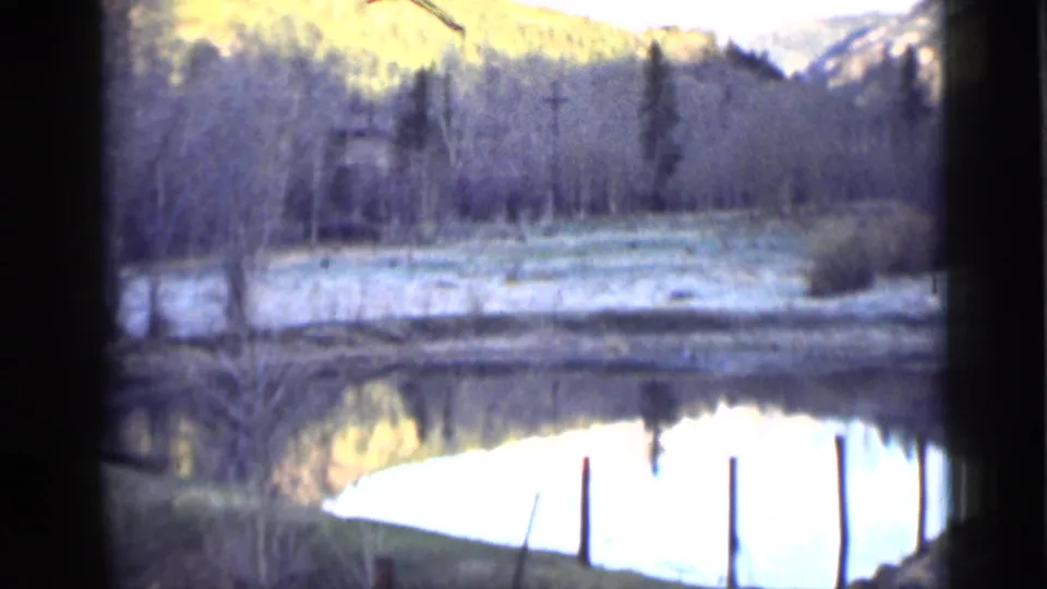 1939 Utah 8mm frame showing a small reflective lake bordered by bare trees, brush, and low hills in soft light.