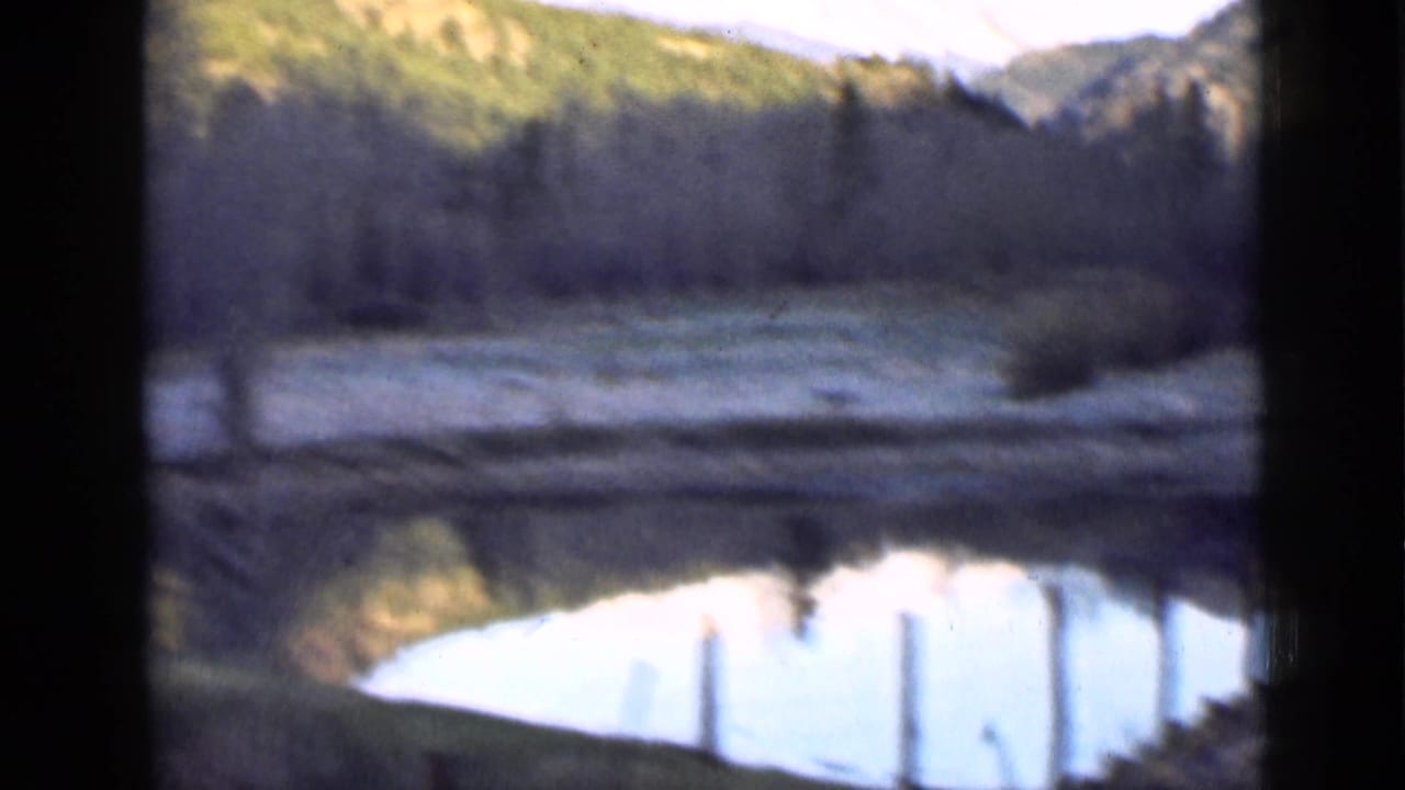 Pond reflecting pale sky below wooded Utah mountain slopes, seen through dark window framing.