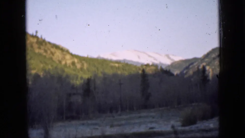 1939 Utah home-movie frame of a still pond, dark foreground framing, evergreen hillsides, bare trees, and distant snow-capped mountain peaks.