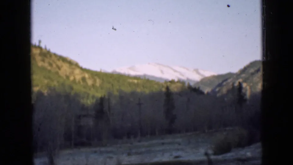 1939 Utah home-movie view of a mountain valley, snow-capped peaks, forested hills, and dark framing edges in soft 8mm color.