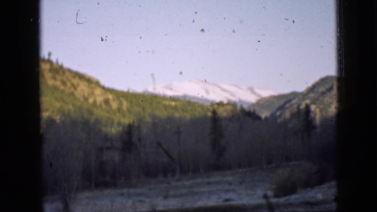 Similar mountain valley view with snowy peaks, forested hills, and dark vertical frame borders.