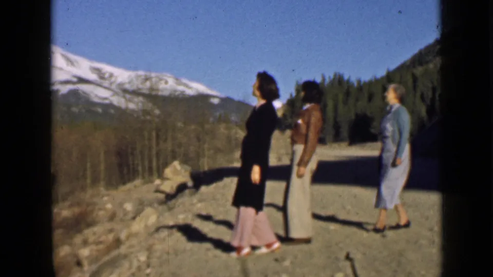Three women in 1939 Utah vacation footage stand near a mountain road or overlook, with snow-capped peaks and trees behind them.