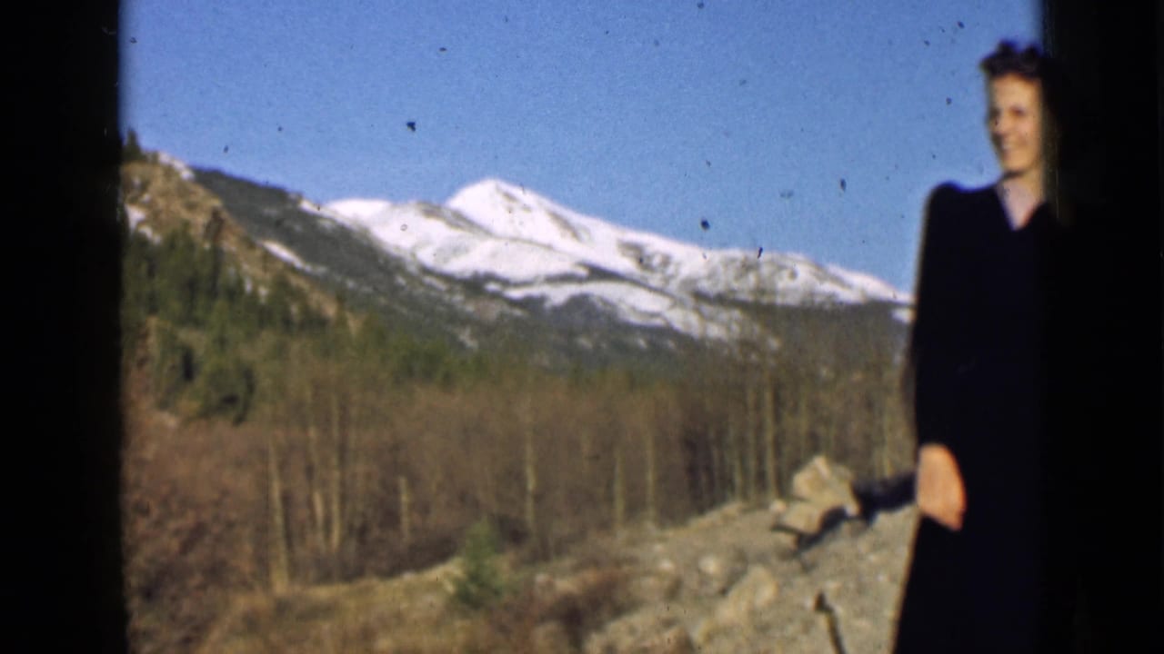 A smiling woman appears at the right edge of a 1939 Utah mountain view, with snowy peaks and wooded slopes behind her.