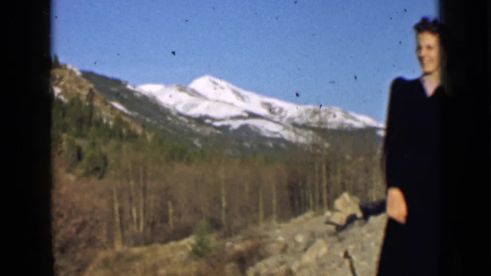 A smiling woman appears at the right edge of a 1939 Utah mountain view, with snowy peaks and wooded slopes behind her.