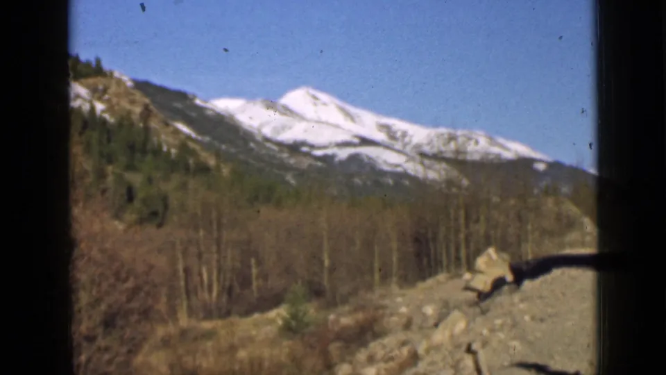 A 1939 Utah home-movie frame shows snowy mountains, wooded slopes, bare trees, and roadside rocks without people visible.