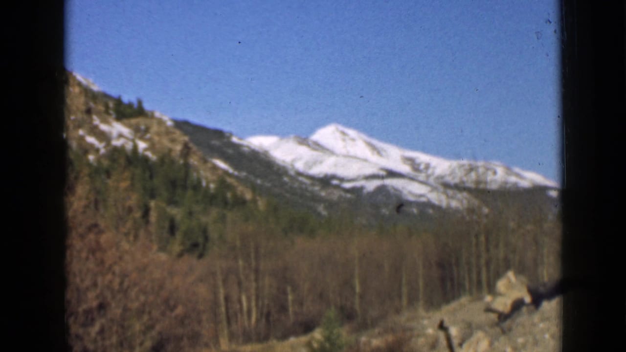 Snow-capped mountain peaks seen through dark vehicle-window framing.