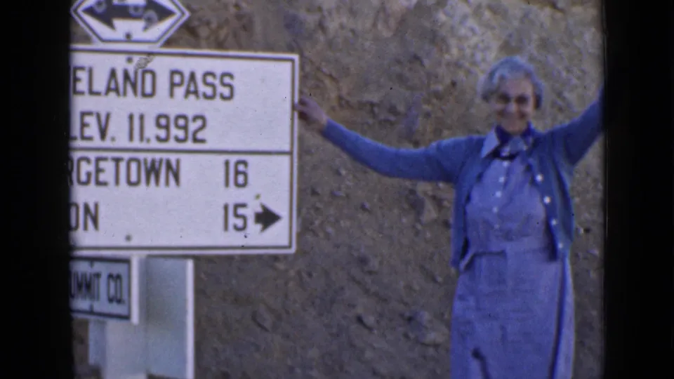 The woman stands proudly next to the Loveland Pass sign, framed by the rocky roadside and vintage 8mm film edges.