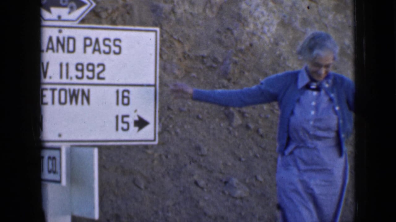 Woman in blue clothing stands beside a roadside directional sign on rocky ground.