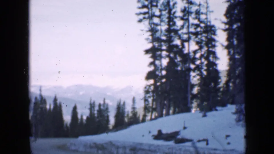 The home-movie view holds on snowy trees and distant mountain ridges, with visible 8mm frame edges.