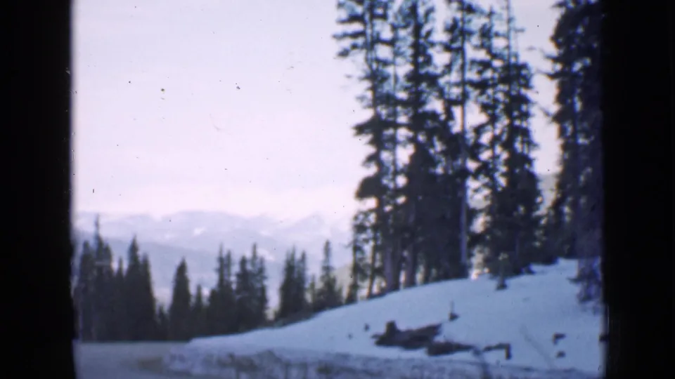 1939 Utah 8mm frame showing a snowy road through evergreens, with distant mountains and dark window or film-frame edges.