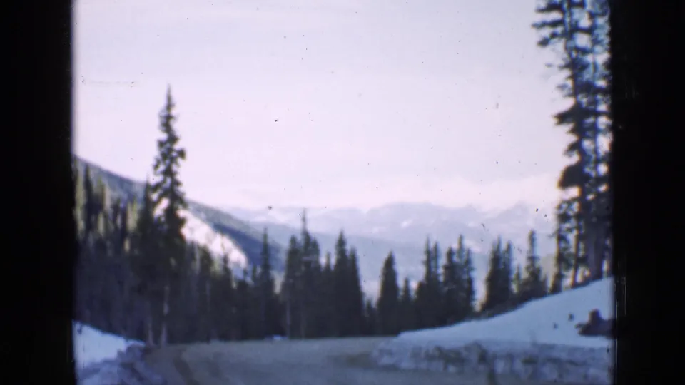 1939 Utah 8mm frame showing a winding snowy road, dense evergreens, soft mountain ridges, and visible film-gate shadow.