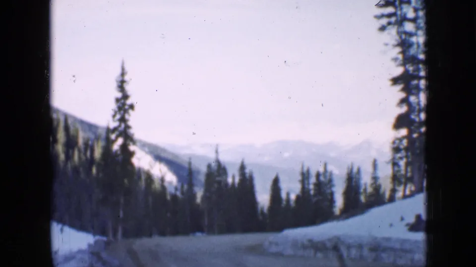 1939 Utah home-movie frame of a snowy mountain road framed by evergreens, with faded color and distant ridgelines visible.