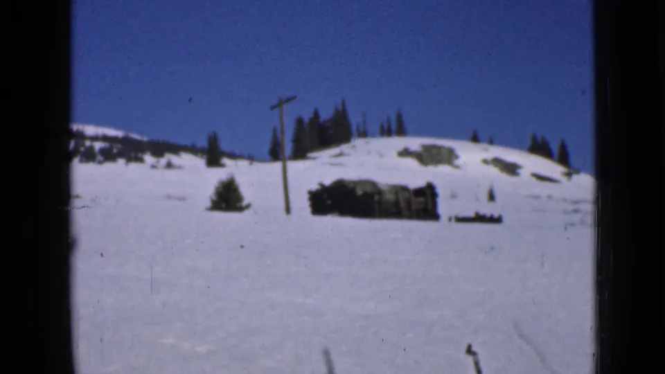 1939 Utah winter frame showing an open snowfield, a utility pole, evergreen trees, and a low weathered wooden structure.