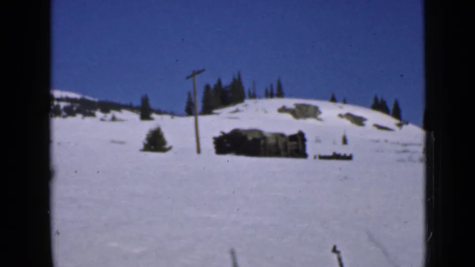 1939 Utah 8mm frame showing a snow-covered mountain slope, utility pole, evergreen trees and a low rustic structure.