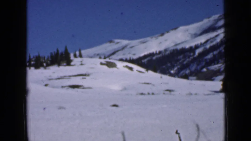 1939 Utah home-movie frame showing a snowy mountain slope, scattered conifers, and blue sky with visible 8mm film edges.