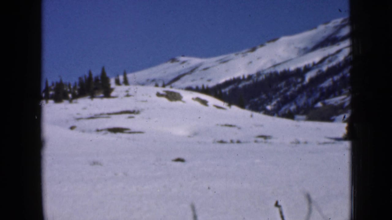 Snowy mountain slope and trees framed by dark 8mm film edges.