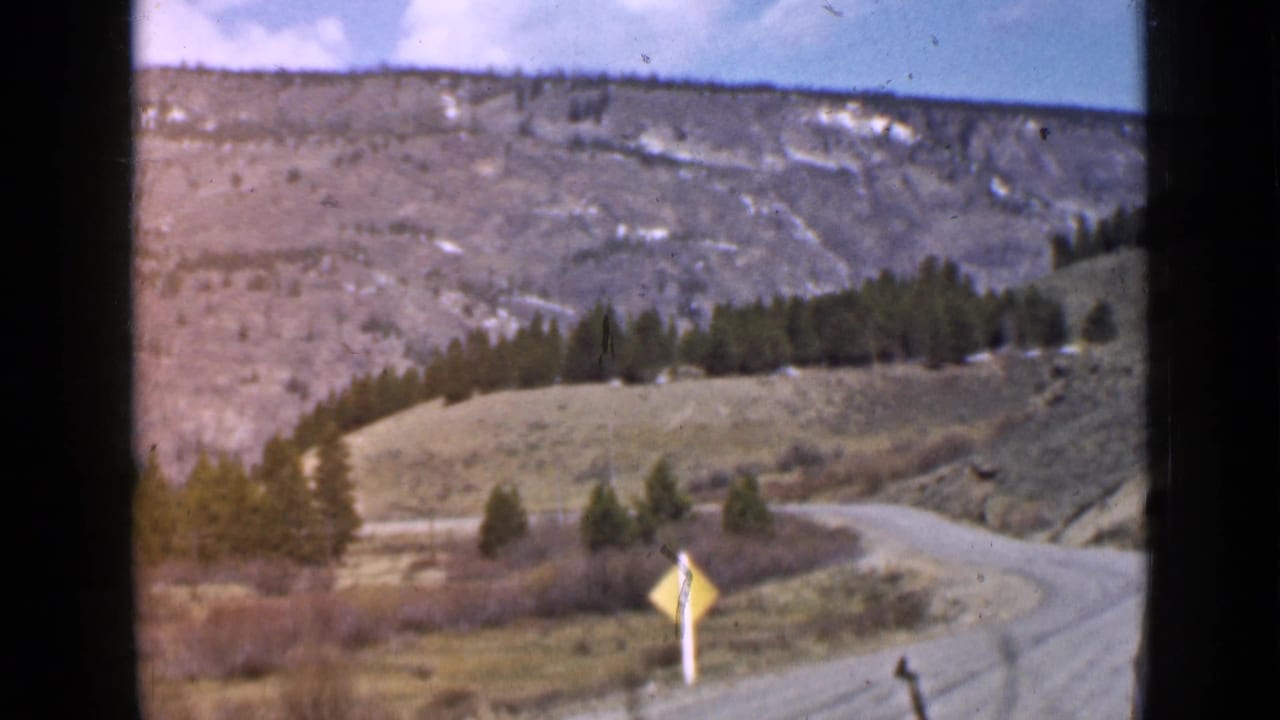 Winding dirt mountain road with a yellow warning sign below rocky slopes.