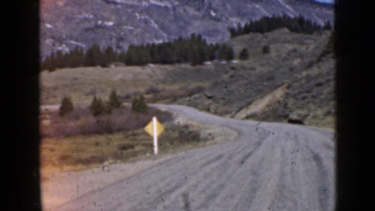 Dirt road curving along a hillside with a yellow roadside sign.