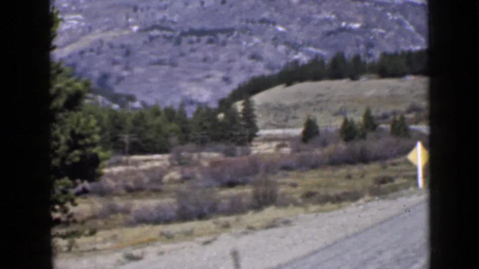 1939 Utah road view from a moving vehicle with a yellow warning sign near the road and layered hills beyond.