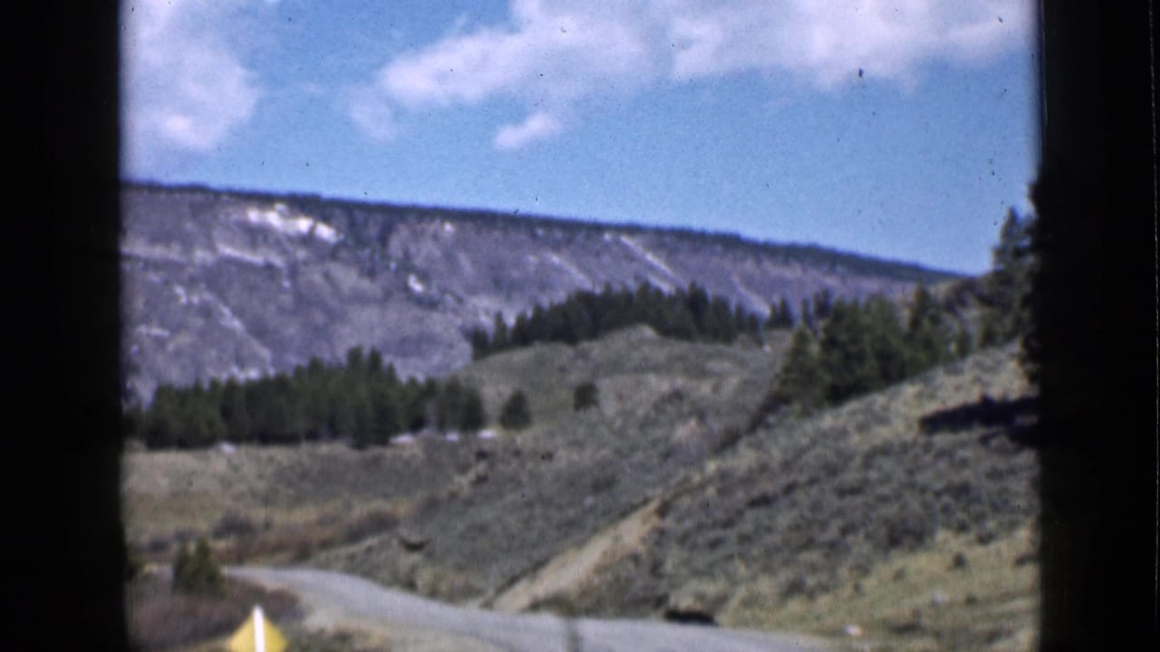 1939 Utah home-movie frame looking along a winding road through scrub hills, evergreens, and a distant mountain ridge.