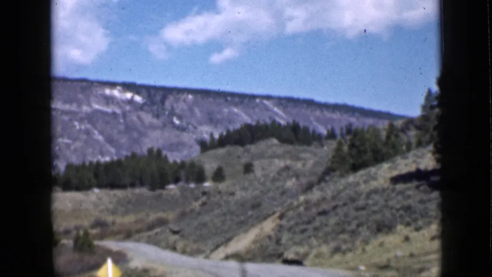 1939 Utah home-movie frame looking along a winding road through scrub hills, evergreens, and a distant mountain ridge.