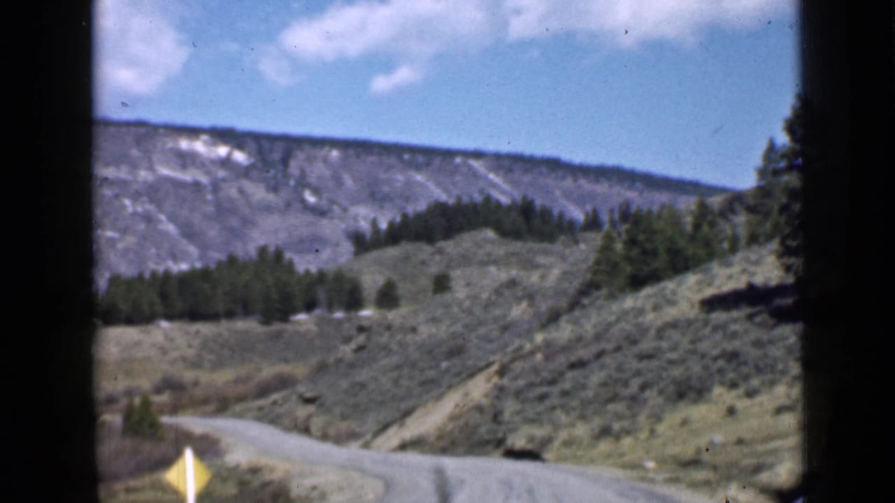 1939 Utah mountain-road view with a yellow roadside sign in the foreground and grey ridges beyond the scrub-covered hills.