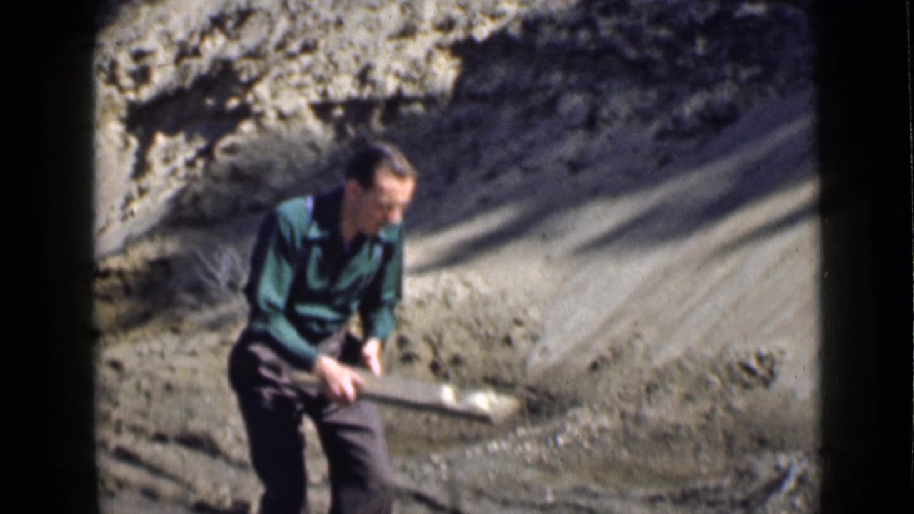 1939 Utah home-movie frame of an adult man handling a long wooden plank beside a dry dirt embankment.