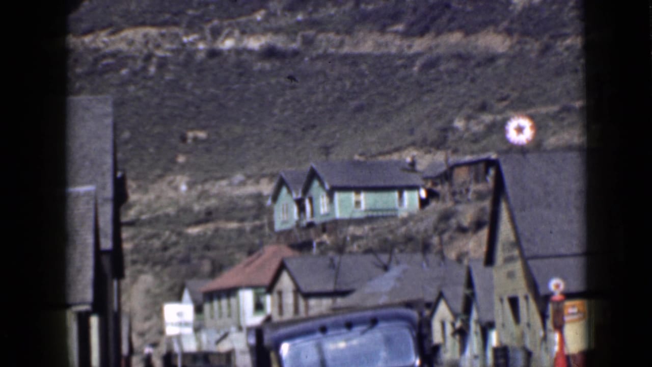 Wider 1939 Utah view of modest hillside houses, a vintage car, utility poles, and a roadside gas pump.