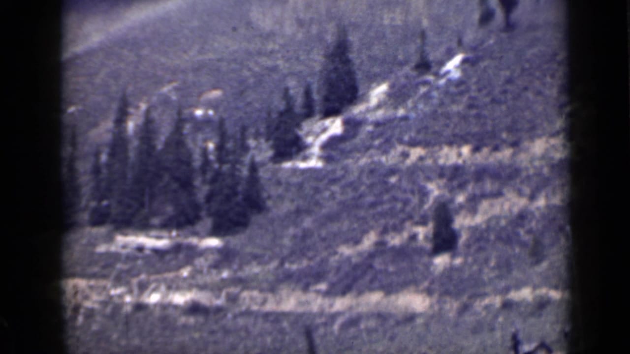 1939 Utah 8mm frame showing a rugged hillside with evergreens, pale snow patches, and a winding track under soft exposure.