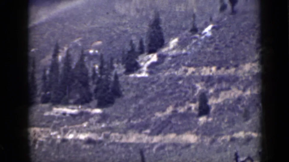 1939 Utah 8mm frame showing a rugged hillside with evergreens, pale snow patches, and a winding track under soft exposure.