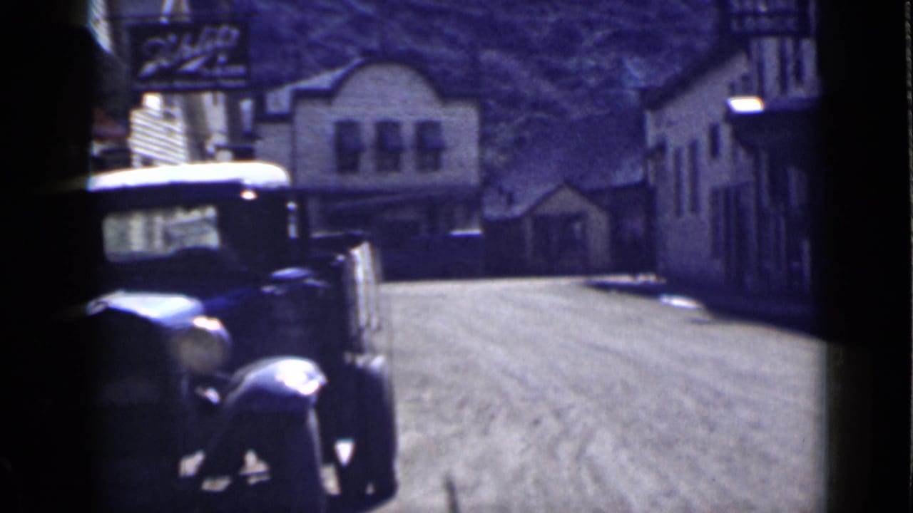 Vintage automobile near a dirt street with buildings and a Shrine Lodge sign behind it.