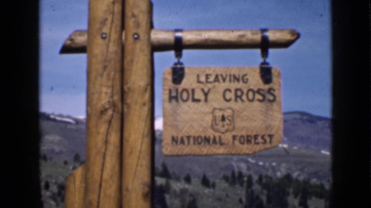 1939 Utah home-movie frame showing a wooden Leaving Holy Cross National Forest sign with the U.S. Forest Service emblem and mountain backdrop.