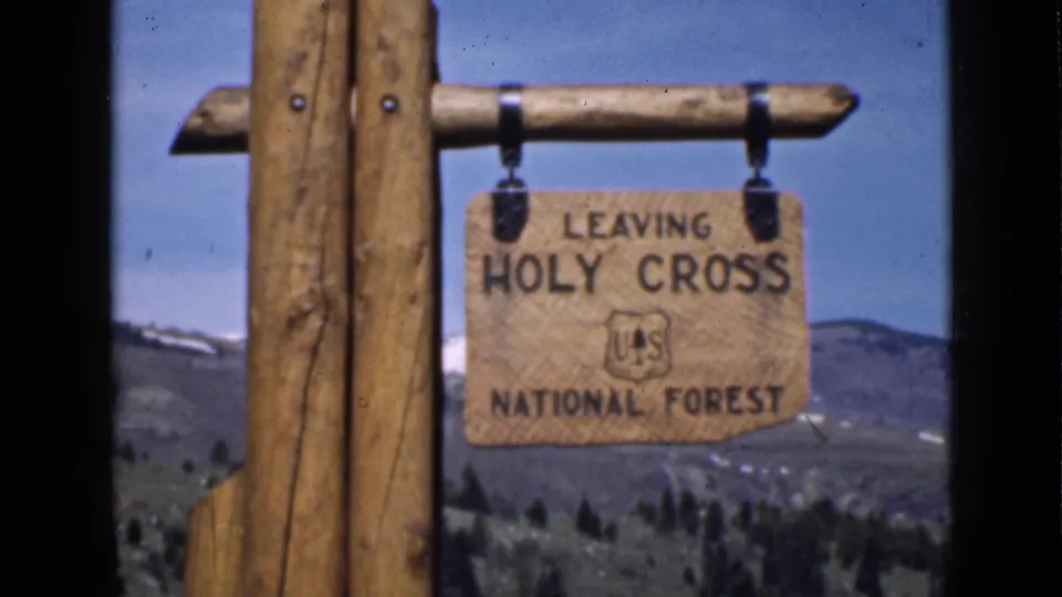 1939 Utah home-movie frame showing a wooden Leaving Holy Cross National Forest sign with the U.S. Forest Service emblem and mountain backdrop.