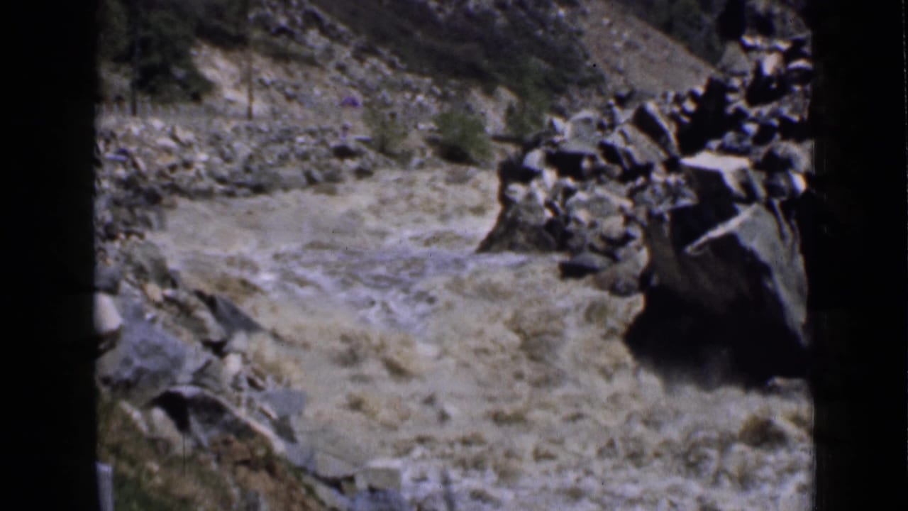 A short 1939 Utah travel shot shows fast muddy water moving through a rocky mountain riverbed with sparse vegetation along the banks.