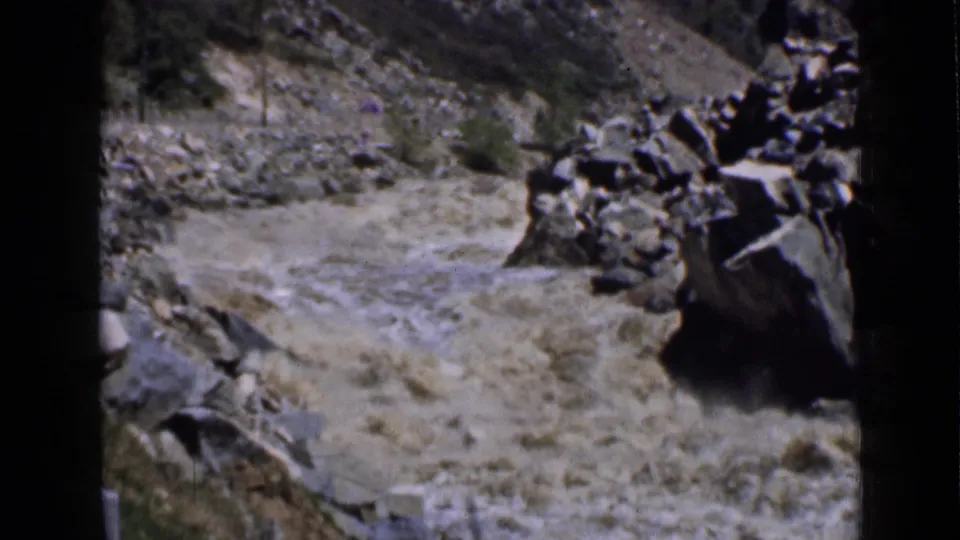 A short 1939 Utah travel shot shows fast muddy water moving through a rocky mountain riverbed with sparse vegetation along the banks.