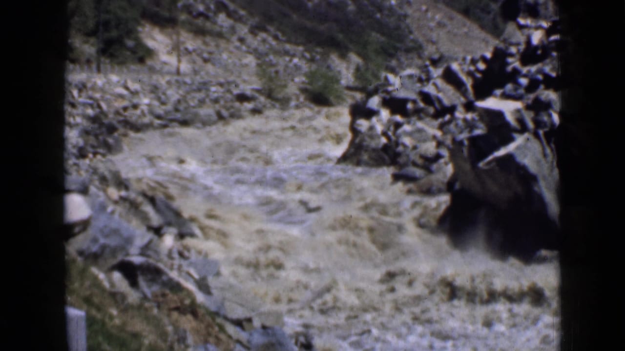 1939 Utah 8mm frame showing turbulent muddy water running past large rocks in a rugged canyon setting.