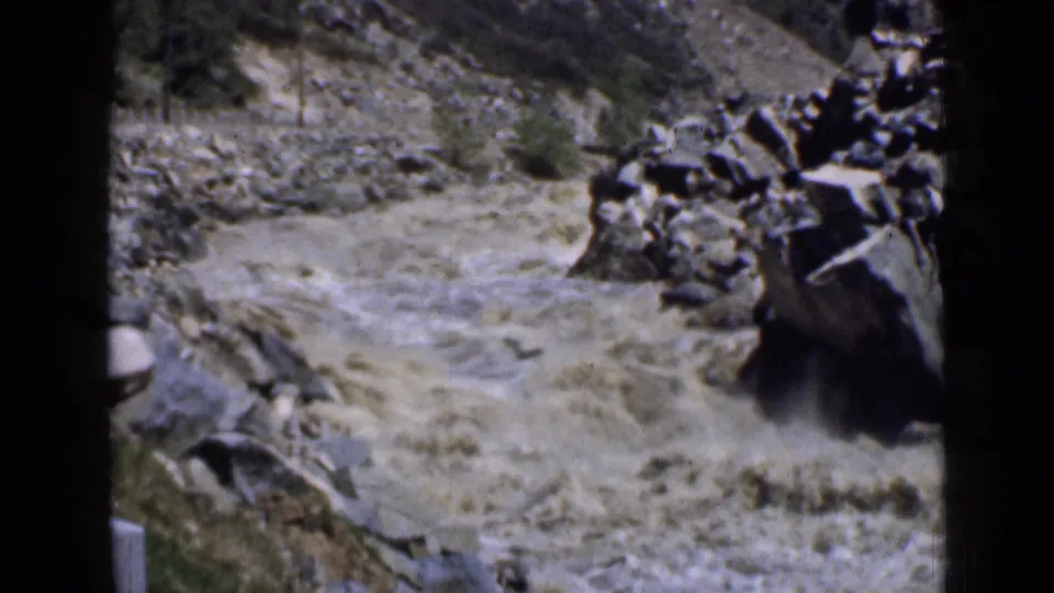 1939 Utah 8mm frame showing turbulent muddy water running past large rocks in a rugged canyon setting.